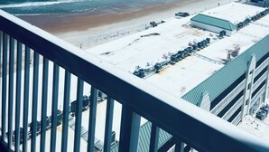 Une vue depuis un balcon donnant sur une plage, avec un espace de stationnement et un bâtiment doté d’un toit végétalisé.