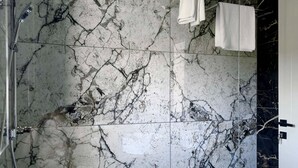 Un baño con piso de mármol, zona de ducha y un perchero con toallas dobladas.