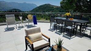 Una terraza con mobiliario exterior, una mesa con botella y vasos, y vistas a las montañas.