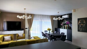 Una sala de estar moderna con un sofá, una mesa de comedor y sillas. Hay un televisor de pantalla plana montado en la pared.