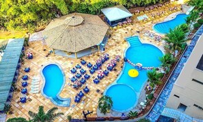 Een resort met meerdere zwembaden, ligbedden en een overdekte paviljoen.