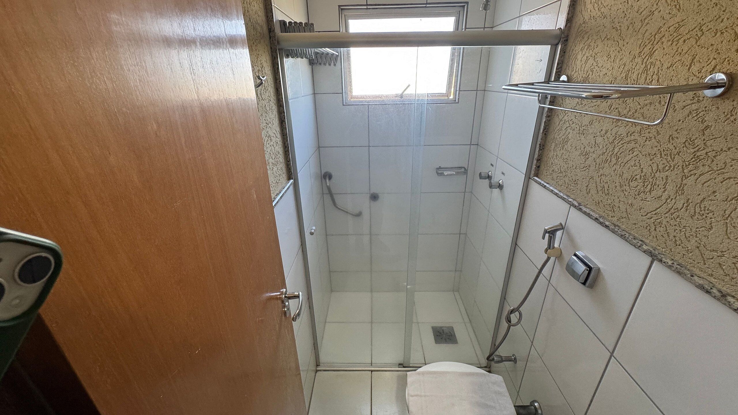 Een kleine badkamer met een douche, een handdoekrek en een raam.