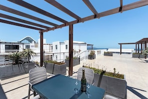 Eine Dachterrasse mit Tisch für zwei Personen, einer Champagnerflasche und Blick aufs Meer.