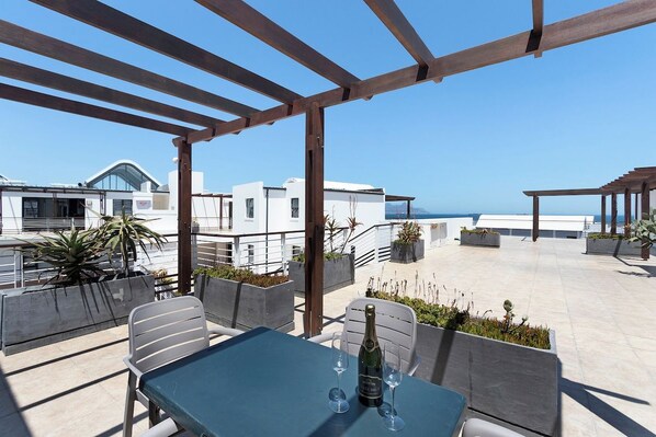 A rooftop terrace with a table set for two, a bottle of champagne, and a view of the sea.