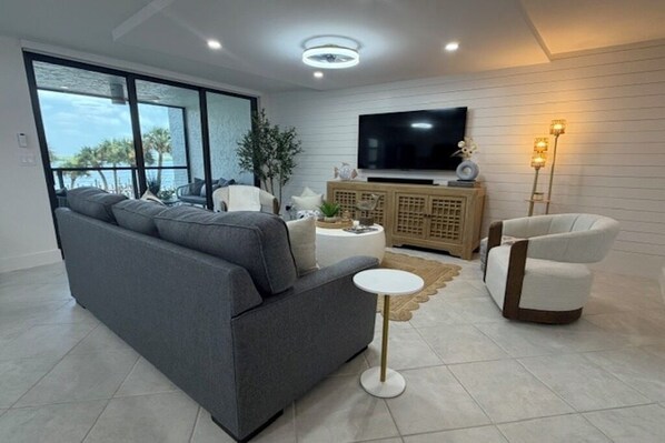 A modern living room with a grey sofa, a white armchair, a small round table, a television, and a floor lamp.