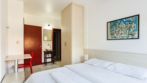 Quarto de hotel com cama, secretária, cadeira, guarda-roupa, casa de banho e um quadro na parede.