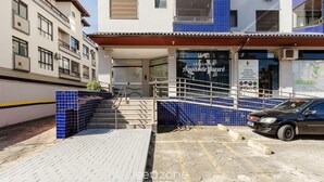 Um edifício com entrada em azulejos azuis, uma escadaria que leva a uma porta e um carro estacionado.