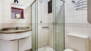 Casa de banho com cabine de duche em vidro, lavatório com bancada de granito e sanita.