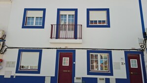 Un immeuble de deux étages avec une porte rouge et des fenêtres dotées de volets blancs.