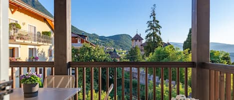 A balcony with a table and chairs, overlooking a mountainous landscape with buildings and greenery.