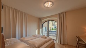 Une chambre d’hôtel avec un lit, un bureau et une vue sur la rue, visible à travers une porte vitrée.