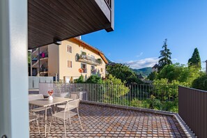 Una terraza con mesa y sillas, vistas a un edificio con balcones y un jardín cercado.