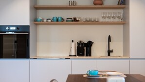 Une cuisine équipée d’un four encastré, d’une machine à café et d’un coin repas avec une table et des chaises.