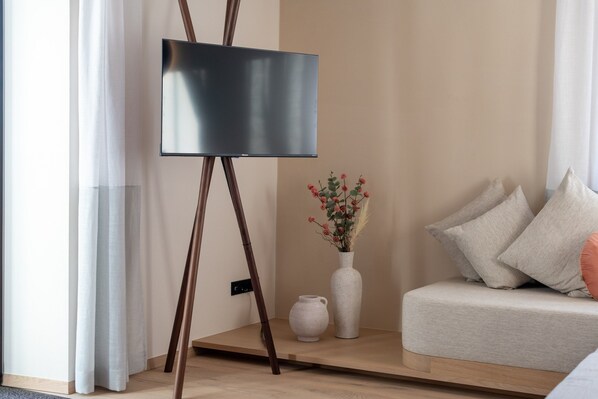 Una habitación minimalista con una televisión de pantalla plana sobre un mueble, un florero blanco con flores y un sofá con cojines.