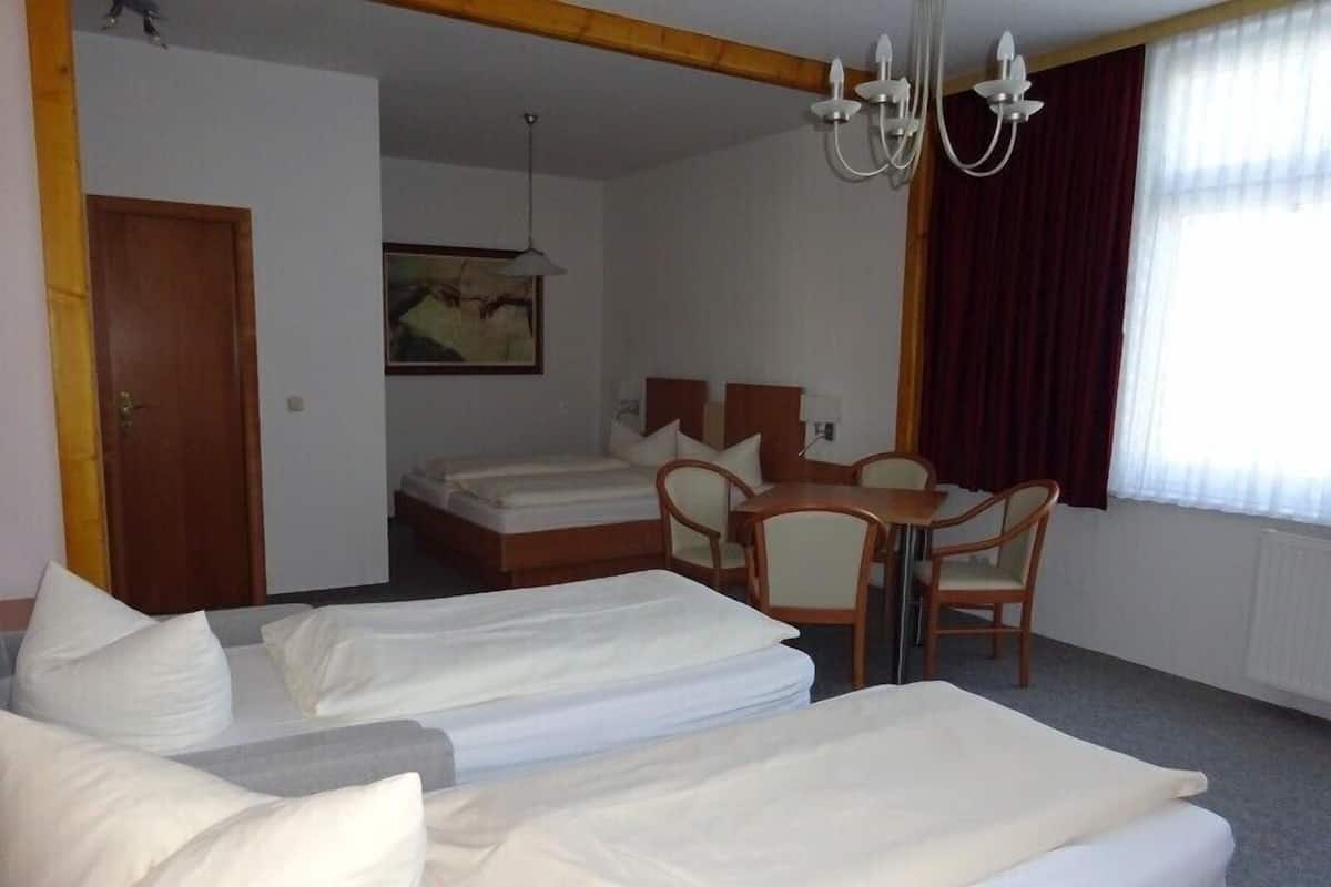 Une chambre d’hôtel avec deux lits simples, une table en bois avec des chaises, un lustre et un tableau au mur.