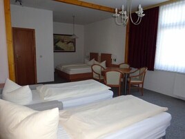 Habitación de hotel con dos camas individuales, una mesa de madera con sillas, una araña y un cuadro en la pared.