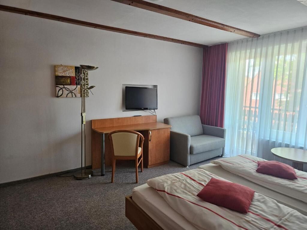Une chambre d’hôtel équipée d’un lit, d’un bureau, d’une chaise, d’une télévision et d’une fenêtre avec des rideaux.