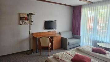 A hotel room with a bed, a desk, a chair, a television, and a window with curtains.