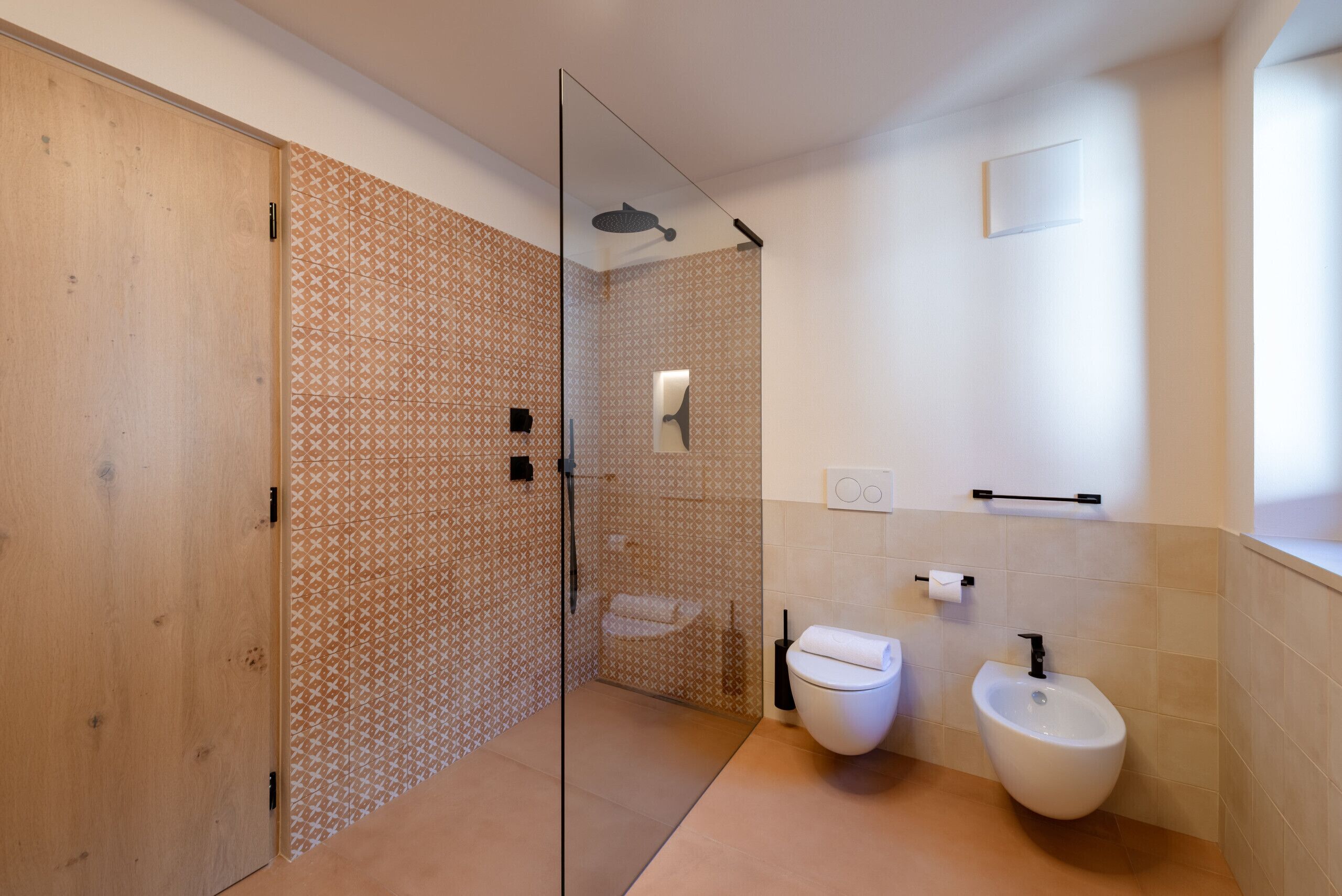 Un bany modern amb plat de dutxa de vidre, un vàter, un bidet i un suport per a tovalloles.