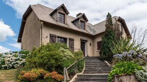 A two-story house with a steep staircase leading to the front door, surrounded by various plants and shrubs. - Villa Delb – Mountain View, Private Pool, and Wi-Fi (Arthez-d'Asson)