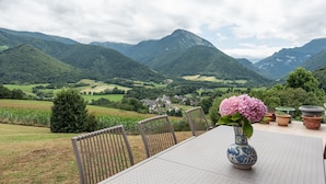 A table with a vase of flowers, chairs, and a view of a valley with mountains. - Villa Delb – Mountain View, Private Pool, and Wi-Fi (Arthez-d'Asson)