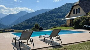Una piscina con dos tumbonas, una casa con techo inclinado y montañas al fondo.