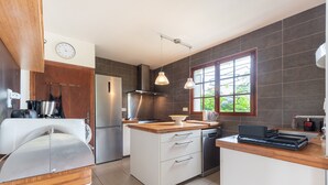 A modern kitchen with a wooden countertop, stainless steel appliances, and a window with a view of greenery. - Villa Delb – Mountain View, Private Pool, and Wi-Fi (Arthez-d'Asson)