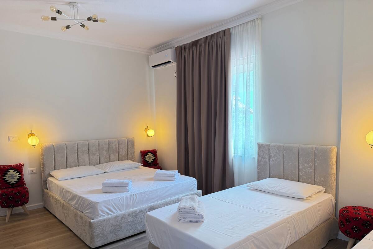 Ein Hotelzimmer mit zwei Betten, einem Deckenventilator, einer Klimaanlage und einem Fenster mit Vorhängen.