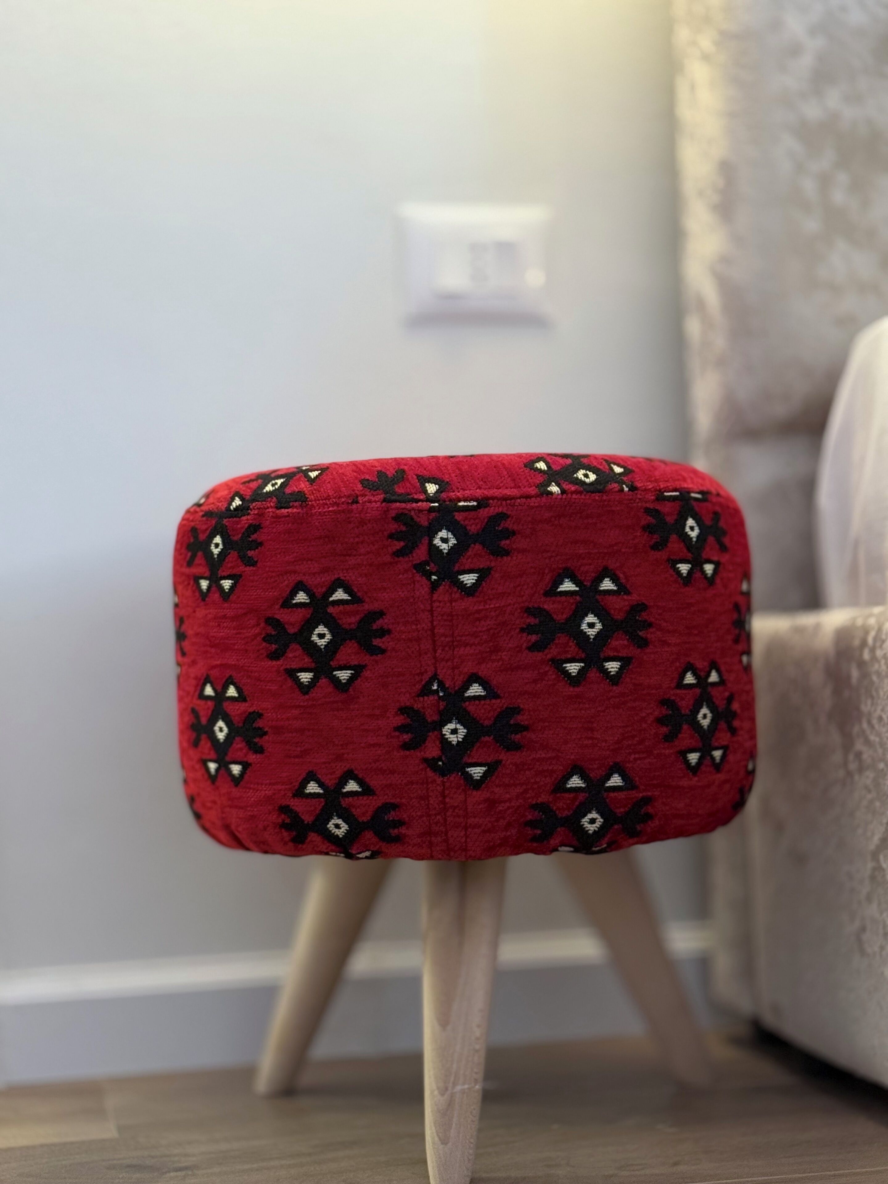 A red ottoman with black and white geometric patterns on a wooden floor.