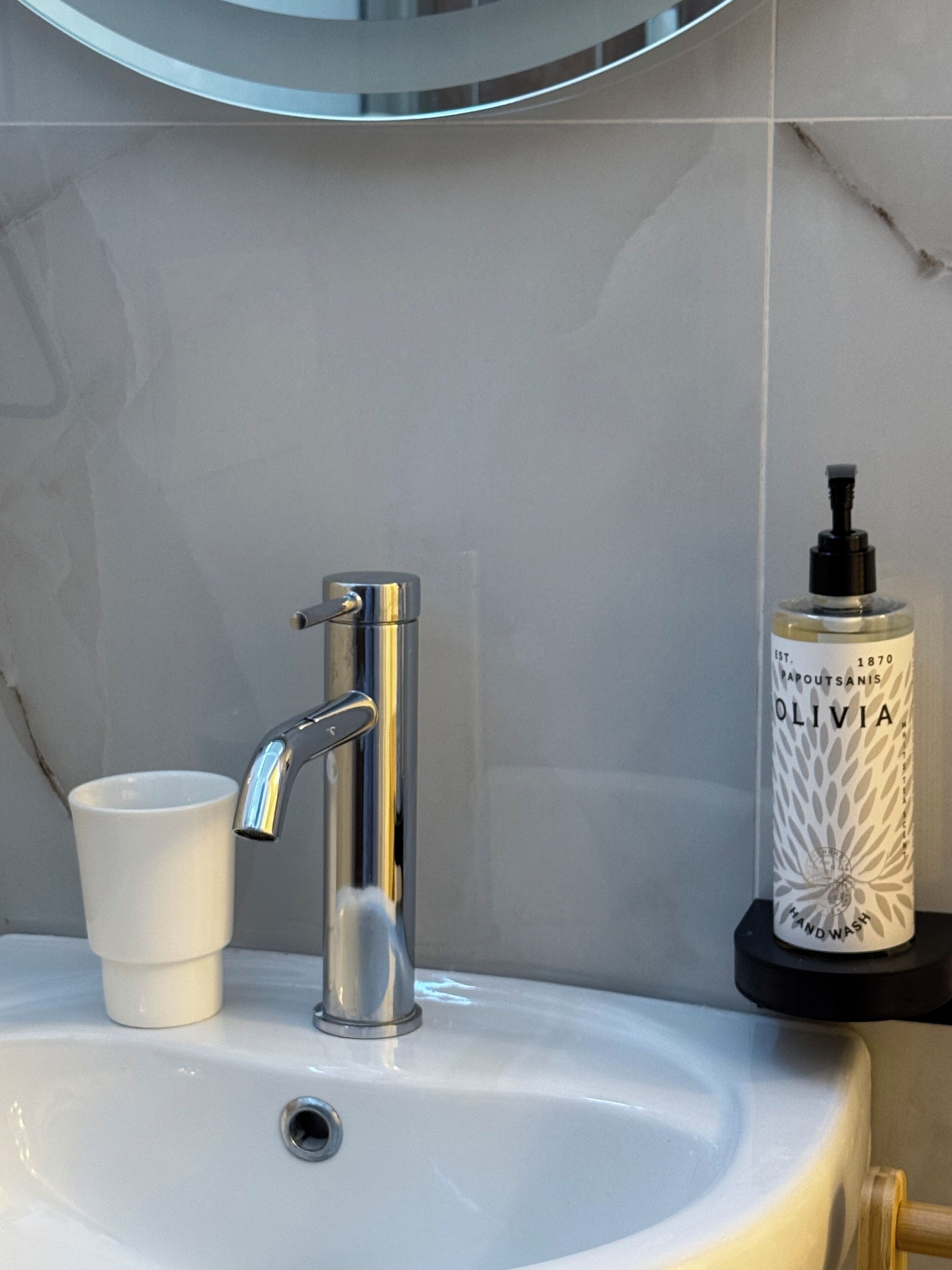 Un lavamanos de baño con un grifo moderno, una taza blanca y una botella de jabón para manos.
