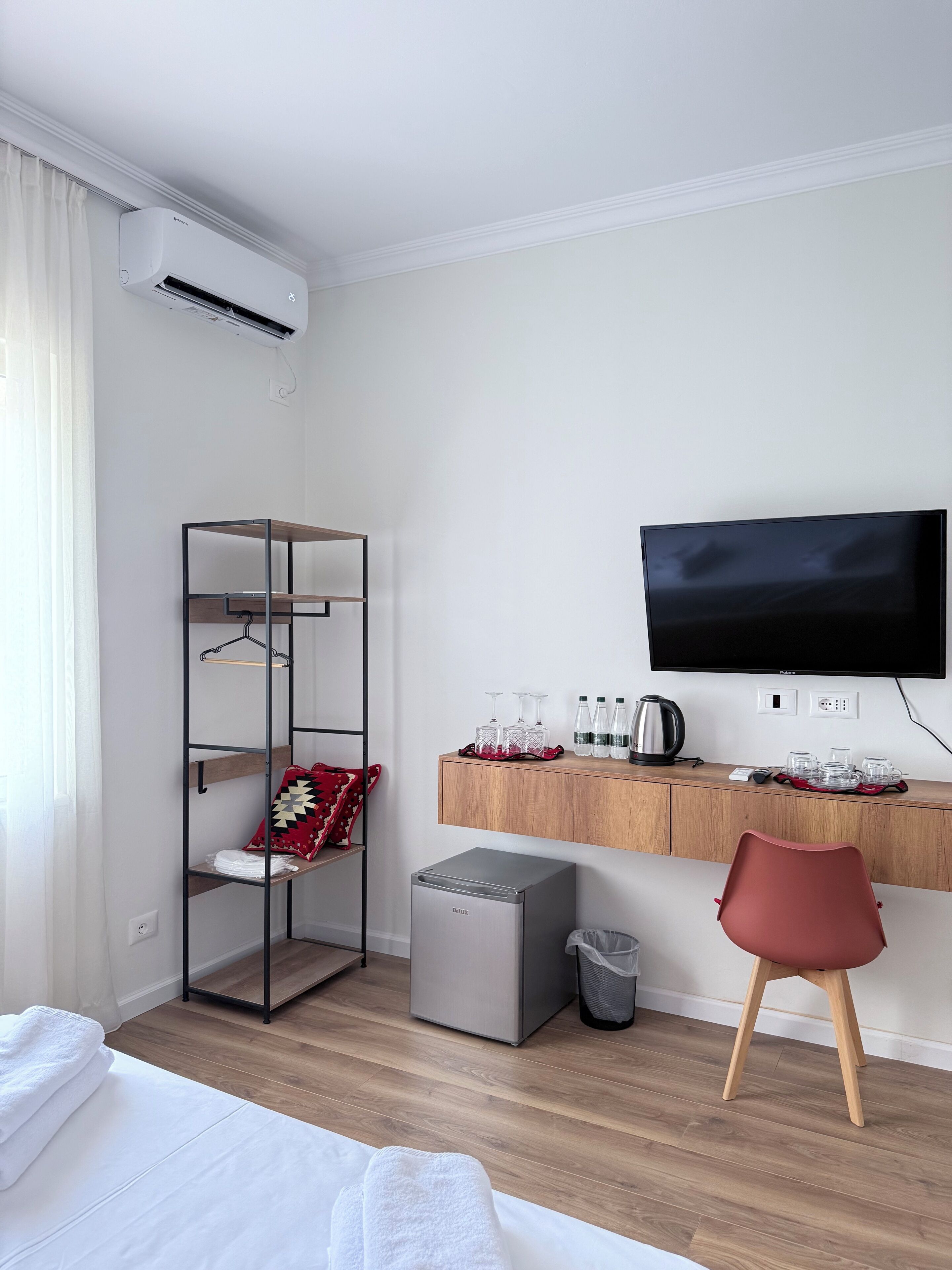 A modern hotel room with a bed, a TV, a desk with a coffee maker, and a wardrobe.
