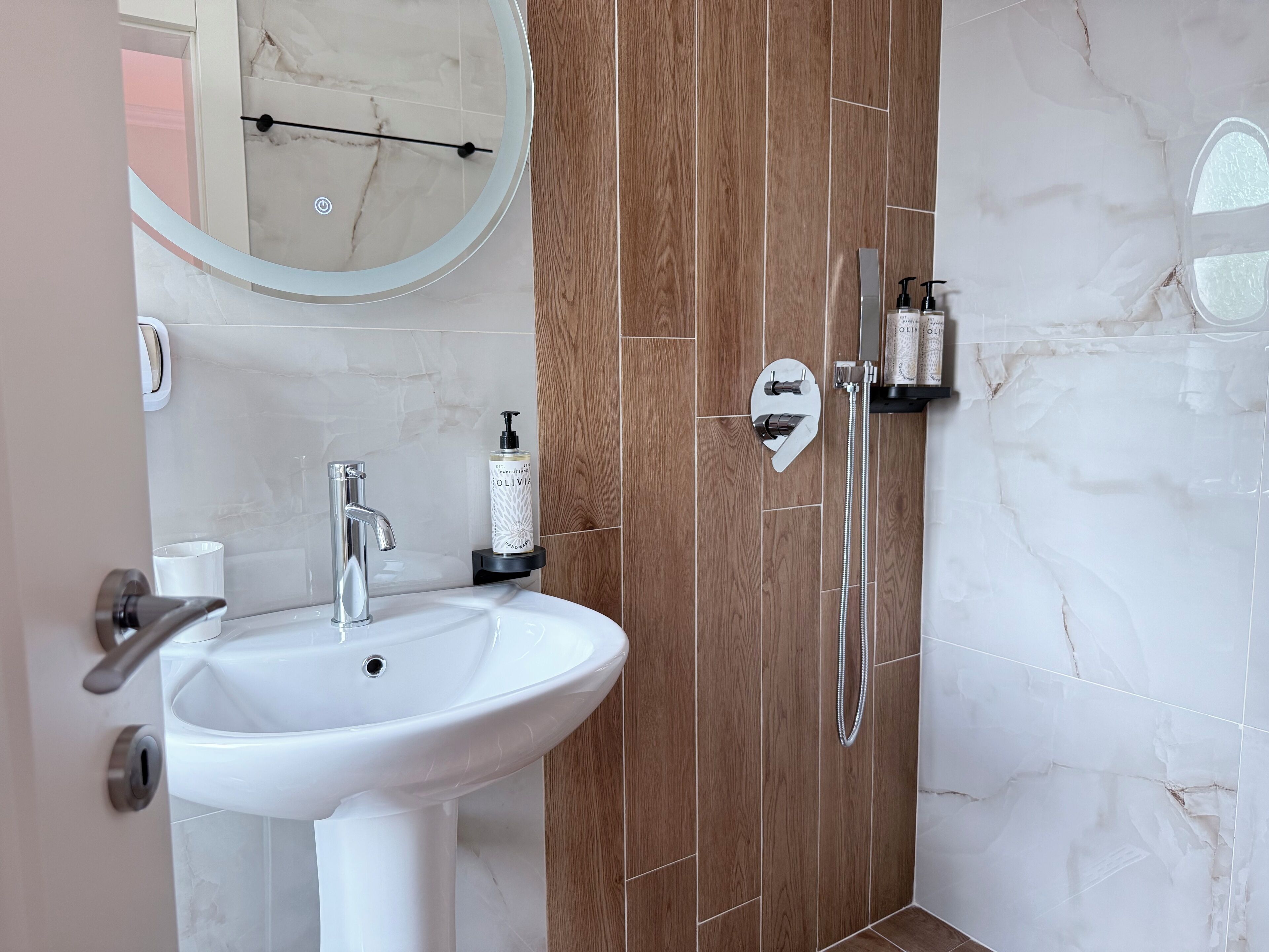 A bathroom with a white sink, a handheld showerhead, and a bottle of shampoo.