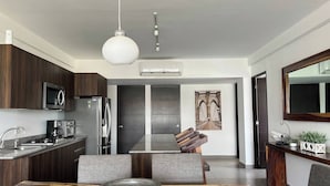 A modern kitchen with dark wood cabinets, stainless steel appliances, and a dining area with a large table and a bowl centerpiece. - Parota Apartment (Nuevo Vallarta)