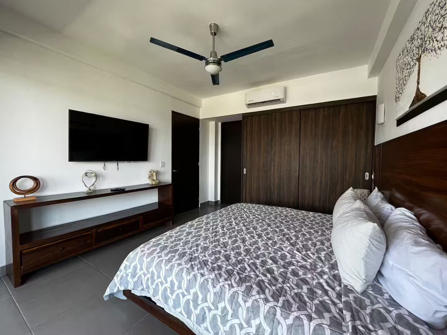A bedroom with a bed, a TV, a ceiling fan, a wardrobe, and an air conditioning unit.