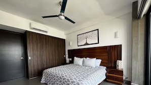A modern bedroom with a large bed, a ceiling fan, a dark wooden wardrobe, and a framed artwork on the wall. - Parota Apartment (Nuevo Vallarta)