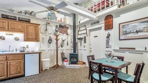 A kitchen with wooden cabinets, a refrigerator, a dining table with chairs, a ceiling fan, and various kitchen utensils and decorations. - Red Barn Village Apartments (Clarks Summit)