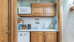 A compact kitchen with wooden cabinets, a white refrigerator, a microwave, and a tiled backsplash. - Red Barn Village Apartments (Clarks Summit)
