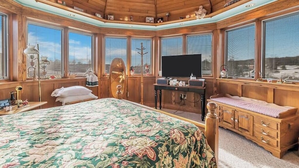 A bedroom with a large bed, a television, wooden cabinets, and large windows. - Red Barn Village Apartments (Clarks Summit)