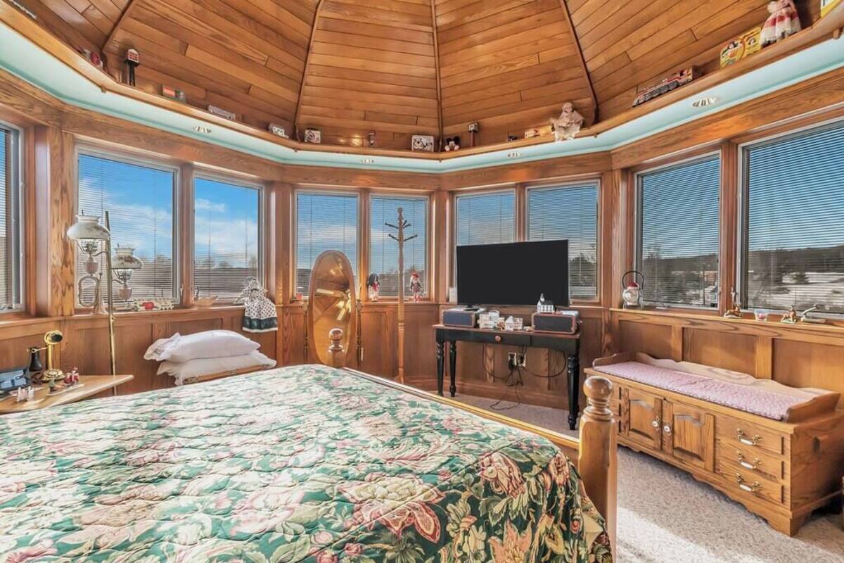 A bedroom with a large bed, a television, wooden cabinets, and large windows.