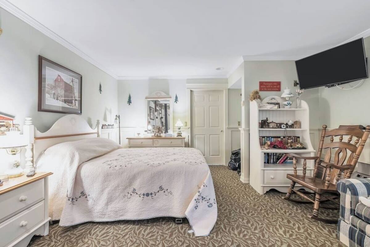 A bedroom with a bed, bedside table, lamp, bookshelf, and a television.