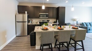 A modern kitchen with dark cabinets, stainless steel appliances, and a marble island with four chairs. - Heartland Flats  (Alliance)