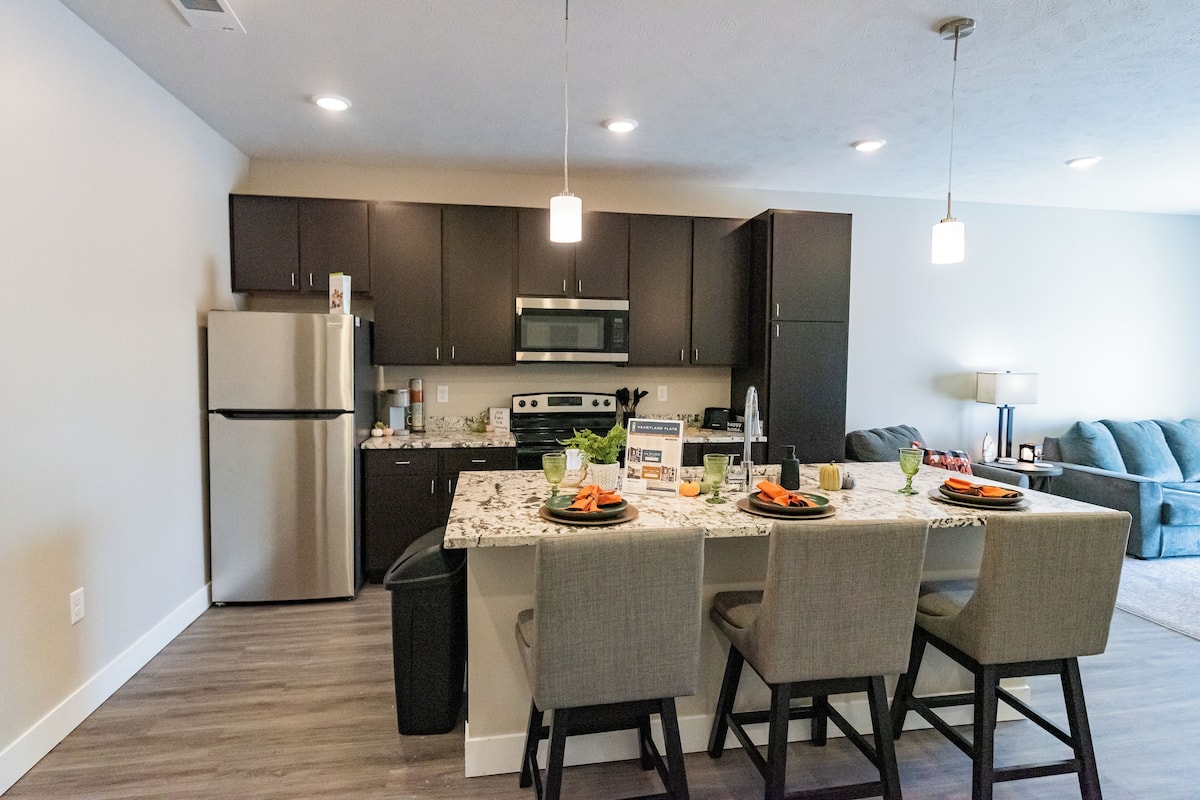 A modern kitchen with dark cabinets, stainless steel appliances, and a marble island with four chairs.