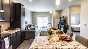 A modern kitchen with dark cabinets, a marble countertop, and a dining area with a long table. - Heartland Flats  (Alliance)