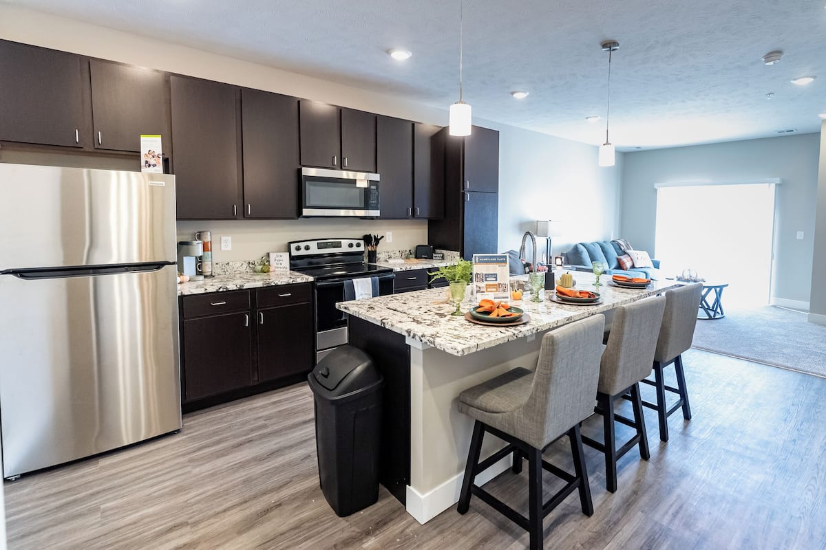 A modern kitchen with dark cabinets, stainless steel appliances, and a marble countertop.
