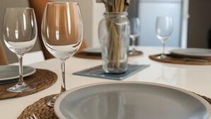 A dining table set with plates, cutlery, and wine glasses, with a vase of dried flowers in the background.