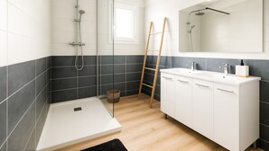 A modern bathroom with a glass shower enclosure, a white vanity with a mirror, and a wooden ladder.