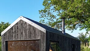 Eine Holzhütte mit einem großen Fenster, einer kleinen Sitzgelegenheit im Freien und einem Whirlpool.