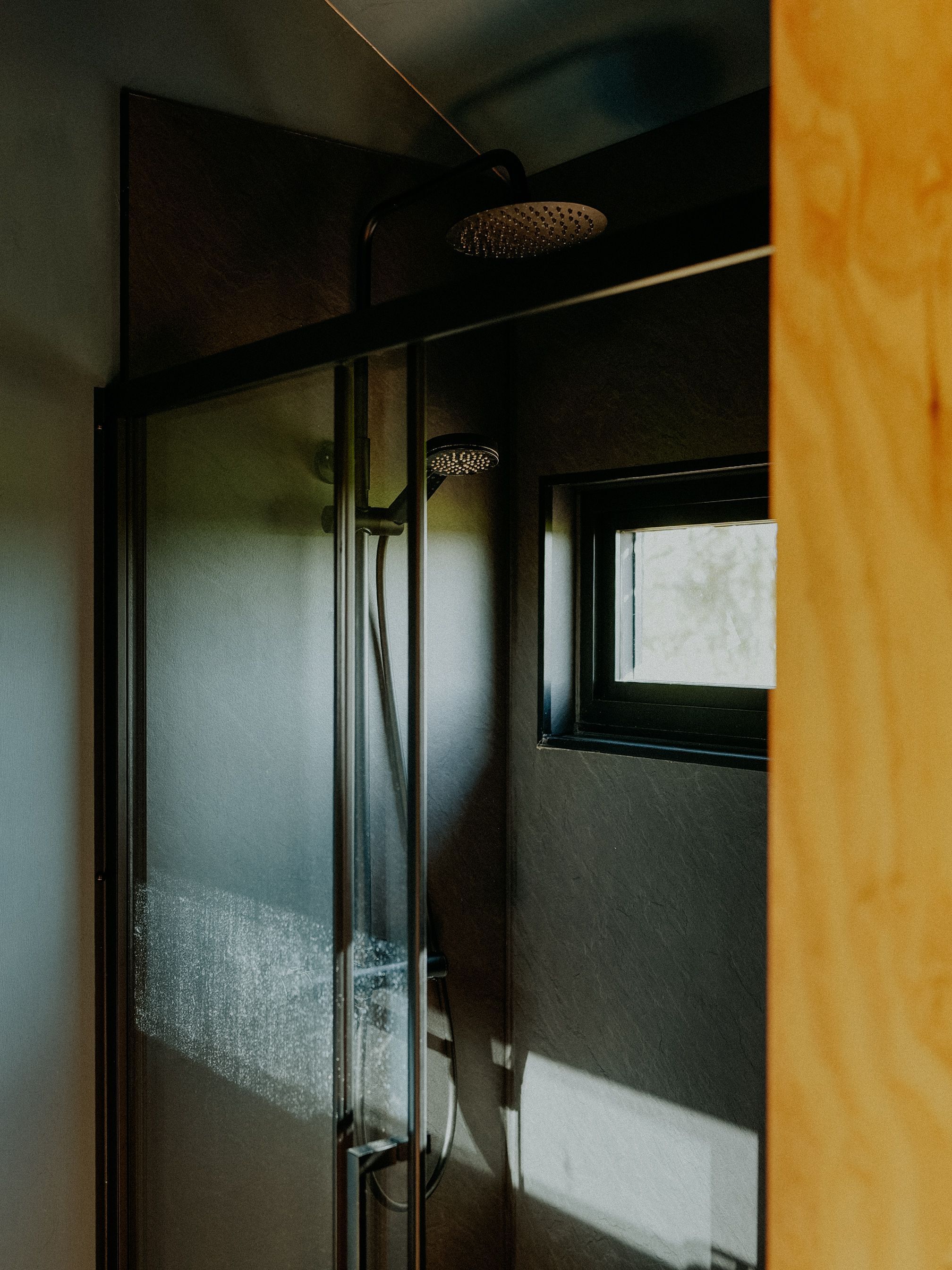 A glass-enclosed shower with a handheld showerhead and a window above it.