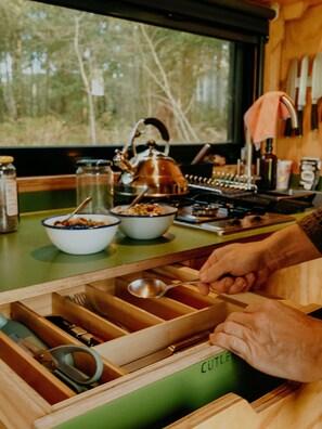 A kitchen with a window view of trees, a kettle, and various kitchen utensils.
