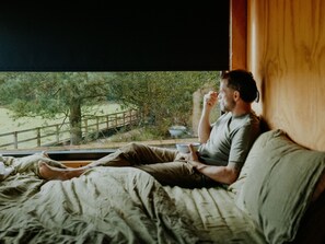 A person sitting on a bed with a window view of a natural landscape.